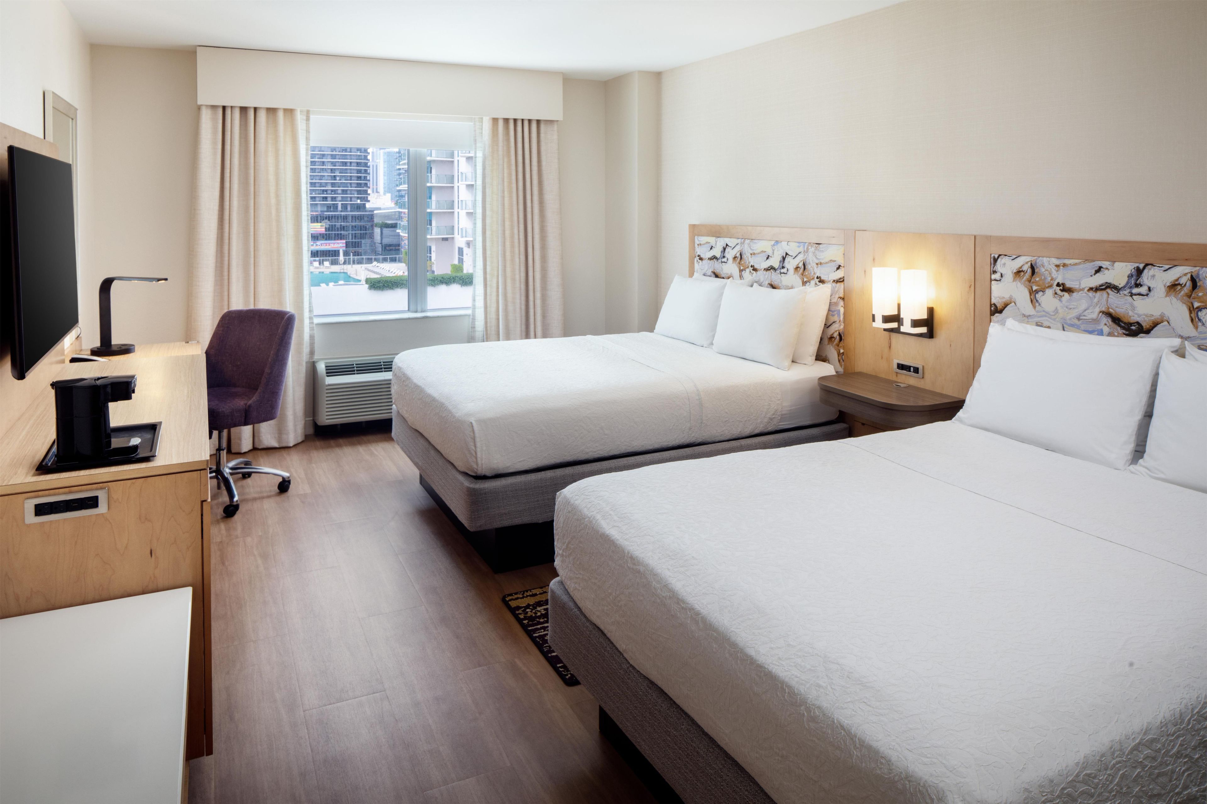 Une chambre d’hôtel avec deux lits, un bureau avec un ordinateur, une chaise et une fenêtre avec des rideaux.