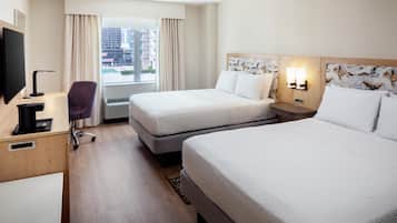 Habitación de hotel con dos camas, un escritorio con computadora, una silla y una ventana con cortinas.