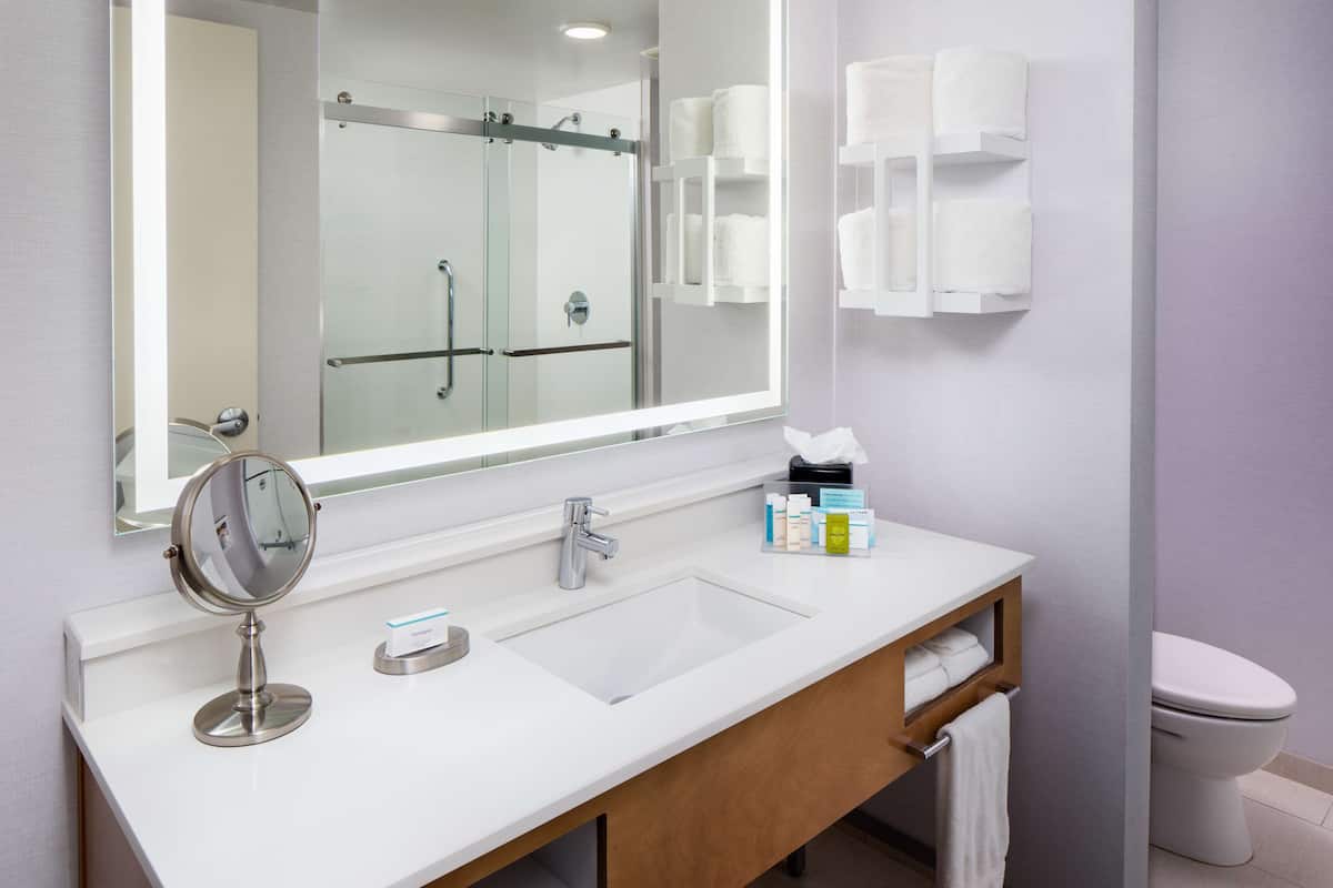 A bathroom with a double sink, a mirror, a toilet, and a glass shower enclosure.