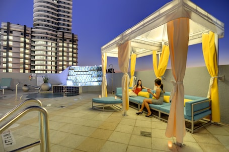 A rooftop pool area with a covered seating area, a pool, and a view of a modern building.