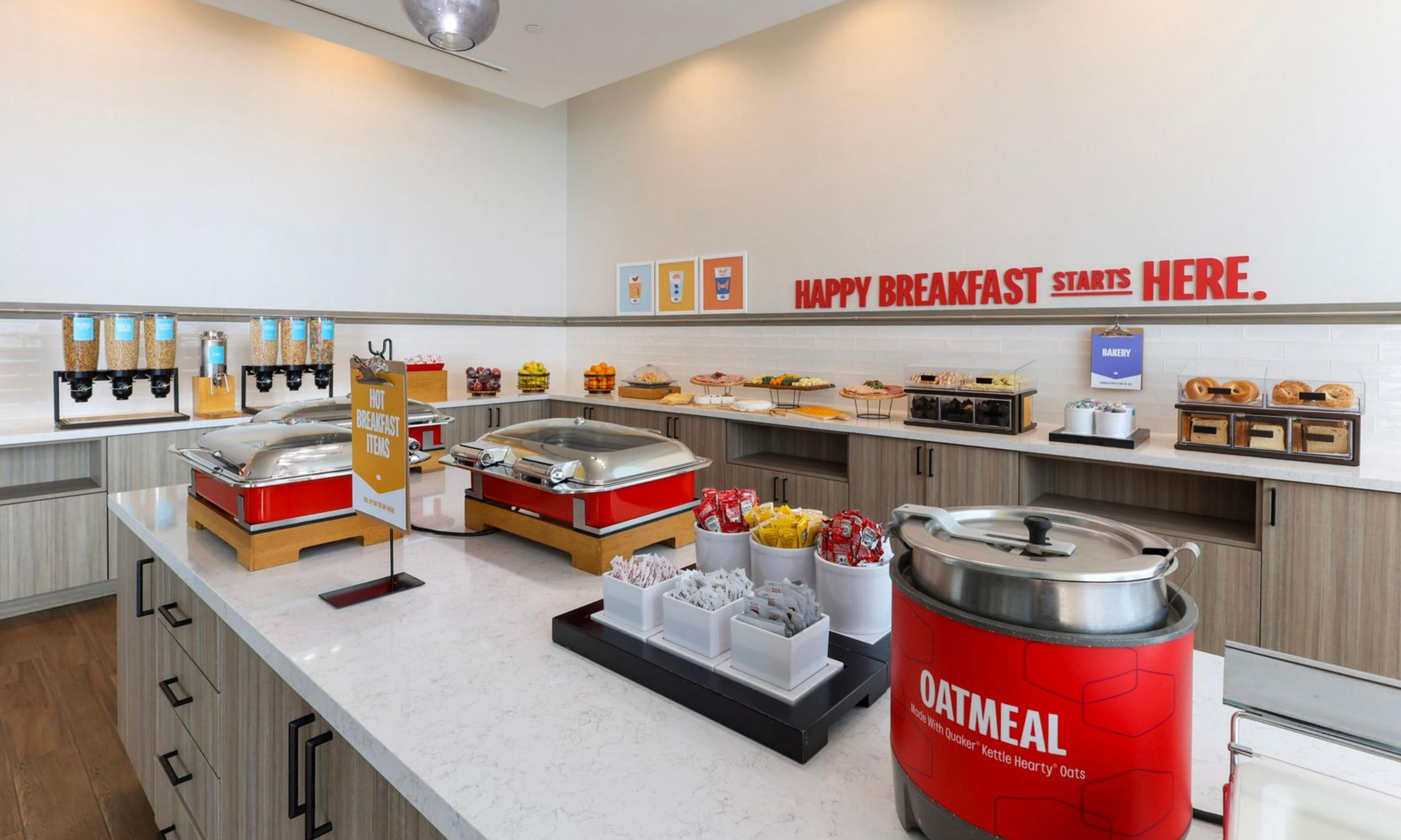 Ein Frühstücksbuffet mit verschiedenen Speisen und einem Schild mit der Aufschrift 'HAPPY BREAKFAST STARTS HERE'.