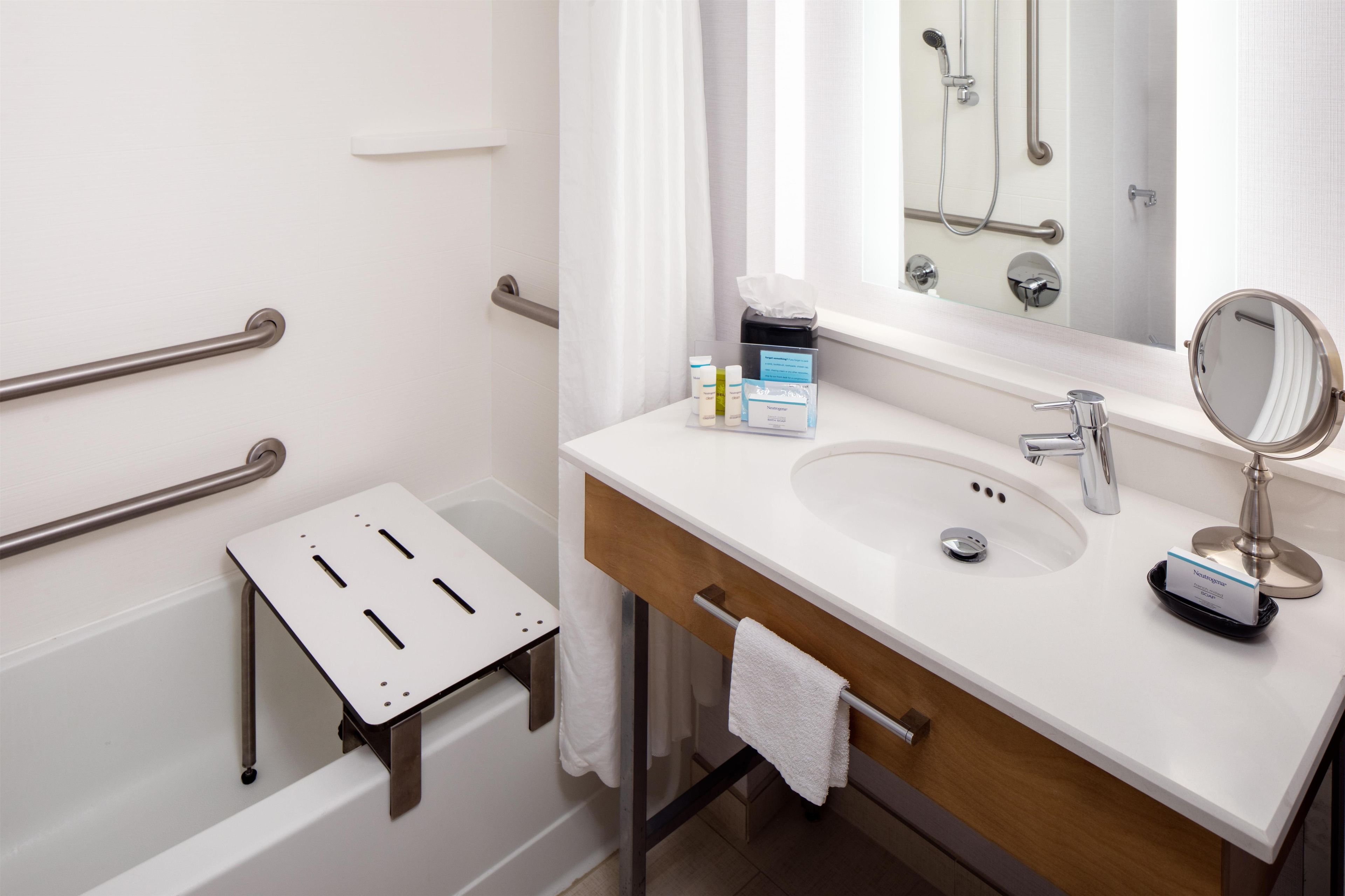 A modern bathroom with a white sink, a mirror, a handheld showerhead, and a small step stool.