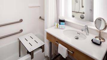A modern bathroom with a white sink, a mirror, a handheld showerhead, and a small step stool.