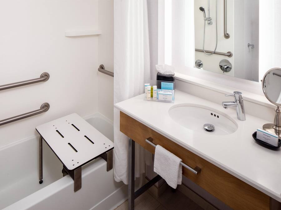 A modern bathroom with a white sink, a mirror, a handheld showerhead, and a small step stool.