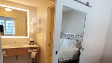Quarto compacto com cama, banheiro com pia e porta de correr para uma varanda.