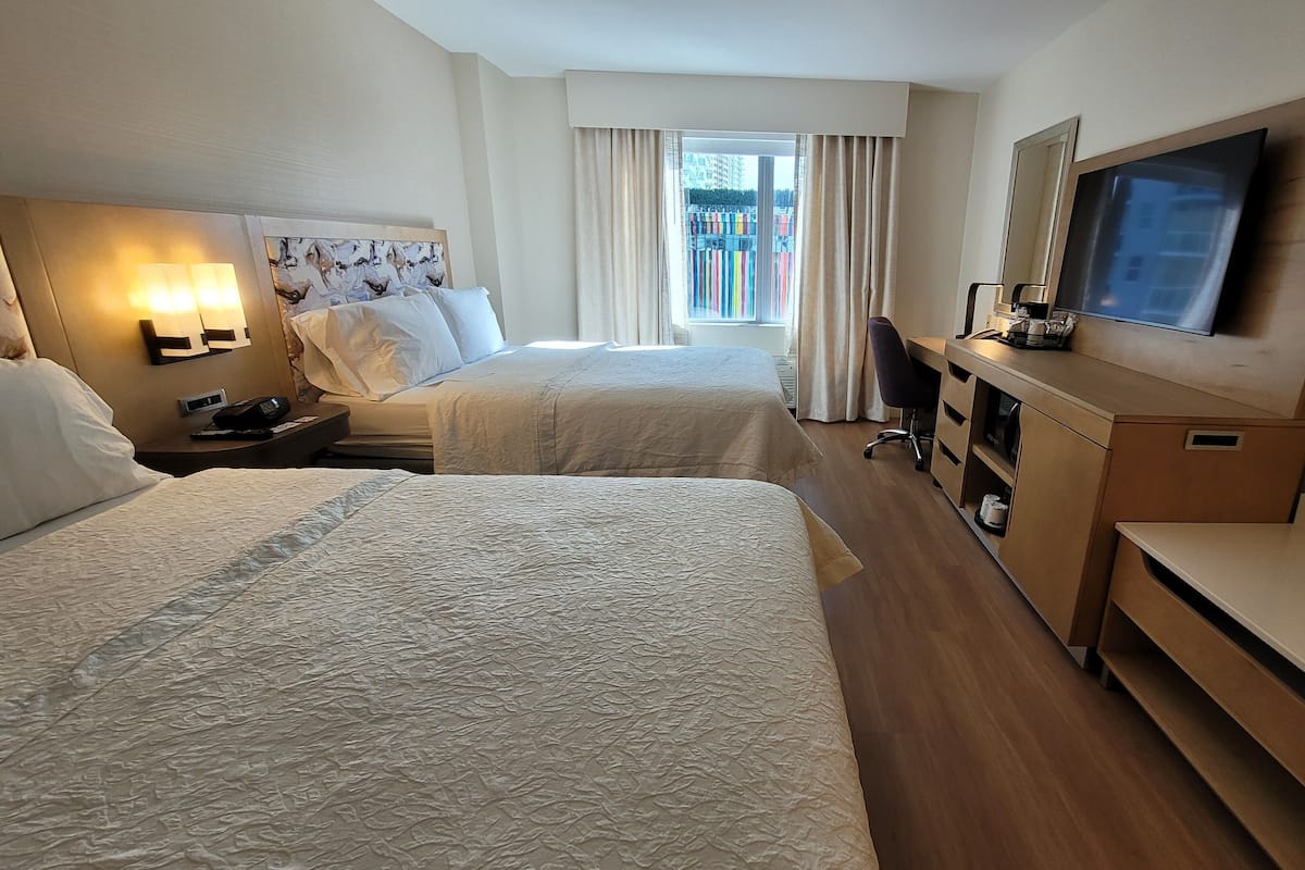 A hotel room with two beds, a desk, a chair, a TV, and a window with curtains.