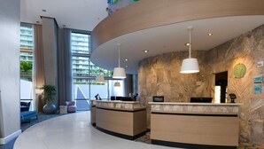 Een hotel receptie met twee balies, een groot raam met uitzicht op gebouwen, en een stenen muur.
