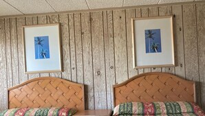 A room with two wooden beds, each with a patterned bedspread. There are framed pictures of palm trees on the wall above the beds. - Glendale Motel (Seaside Heights)