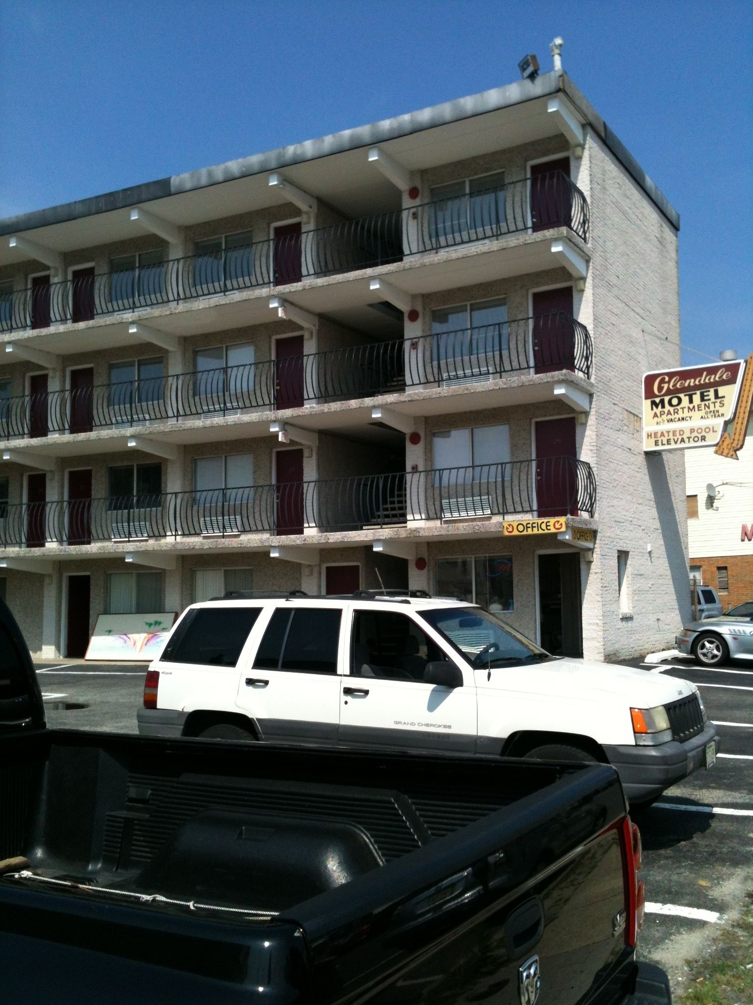 Un motel con varios pisos, balcones y un letrero que indica que ofrece apartamentos, piscina climatizada y ascensor.