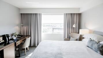 A hotel room with a bed, a desk, a chair, a lamp, and a window with curtains.