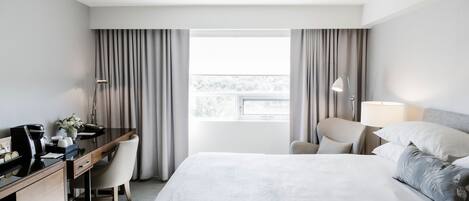 A hotel room with a bed, a desk, a chair, a lamp, and a window with curtains.