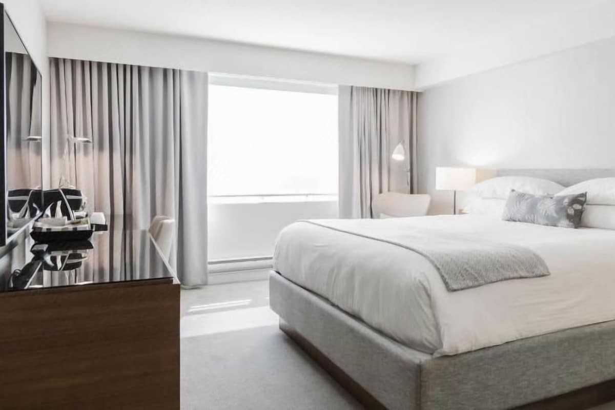 Une chambre d’hôtel moderne, dotée d’un grand lit, de tables de chevet, d’un bureau et offrant une vue sur l’extérieur.