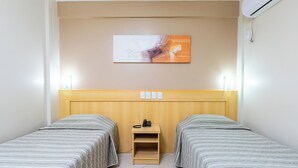 Habitación de hotel con dos camas individuales, cabecero de madera, mesita de noche con teléfono y aire acondicionado de pared.