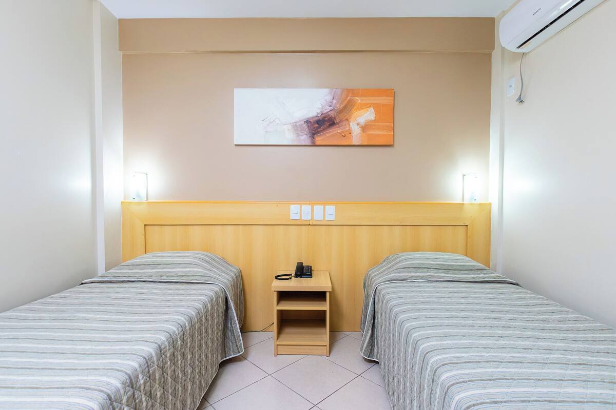 Een hotelkamer met twee eenpersoonsbedden, een houten hoofdbord, een nachtkastje met een telefoon en een wandairconditioner.