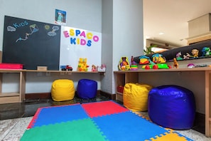 Ein Kinderspielbereich mit einer Tafel, Spielzeug, Sitzsäcken und einer bunten Spielecke.
