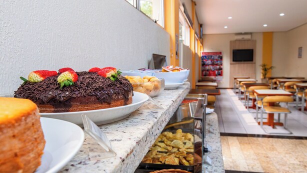 Un bufé con diversos alimentos, entre ellos un pastel de chocolate con fresas, y una zona de estar con mesas y sillas.