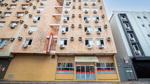 Un edificio de varios pisos con numerosas unidades de aire acondicionado, una entrada a nivel de calle con toldo rojo y un hidrante visible.