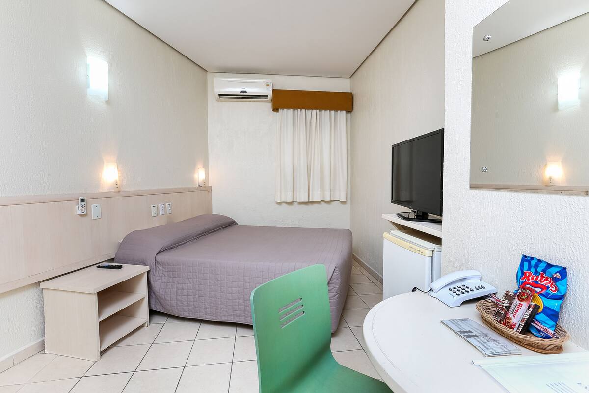 Ein Hotelzimmer mit Bett, Schreibtisch, Stuhl, Fernseher, Telefon und einer Korb mit Snacks.