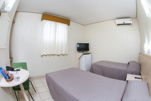 Ett litet hotellrum med två sängar, en TV, ett skrivbord med en stol och ett fönster med gardiner.
