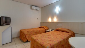 Une chambre avec deux lits, un petit bureau, une télévision et un appareil de climatisation.