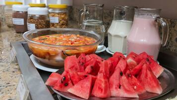 Desayuno con sandía en rodajas, ensalada de frutas y dos jarras de bebidas sobre una encimera de granito.