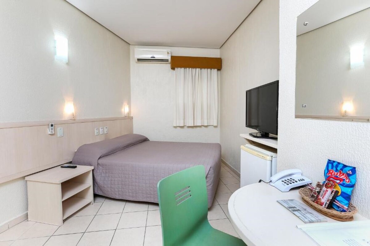 Une chambre d’hôtel équipée d’un lit, d’un bureau, d’une chaise, d’une télévision, d’un téléphone et d’un panier contenant des en-cas.