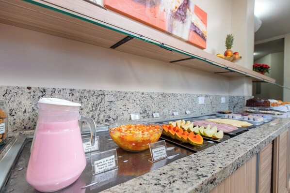 A buffet counter with a pitcher of pink beverage, a bowl of fruit salad, and various food items.