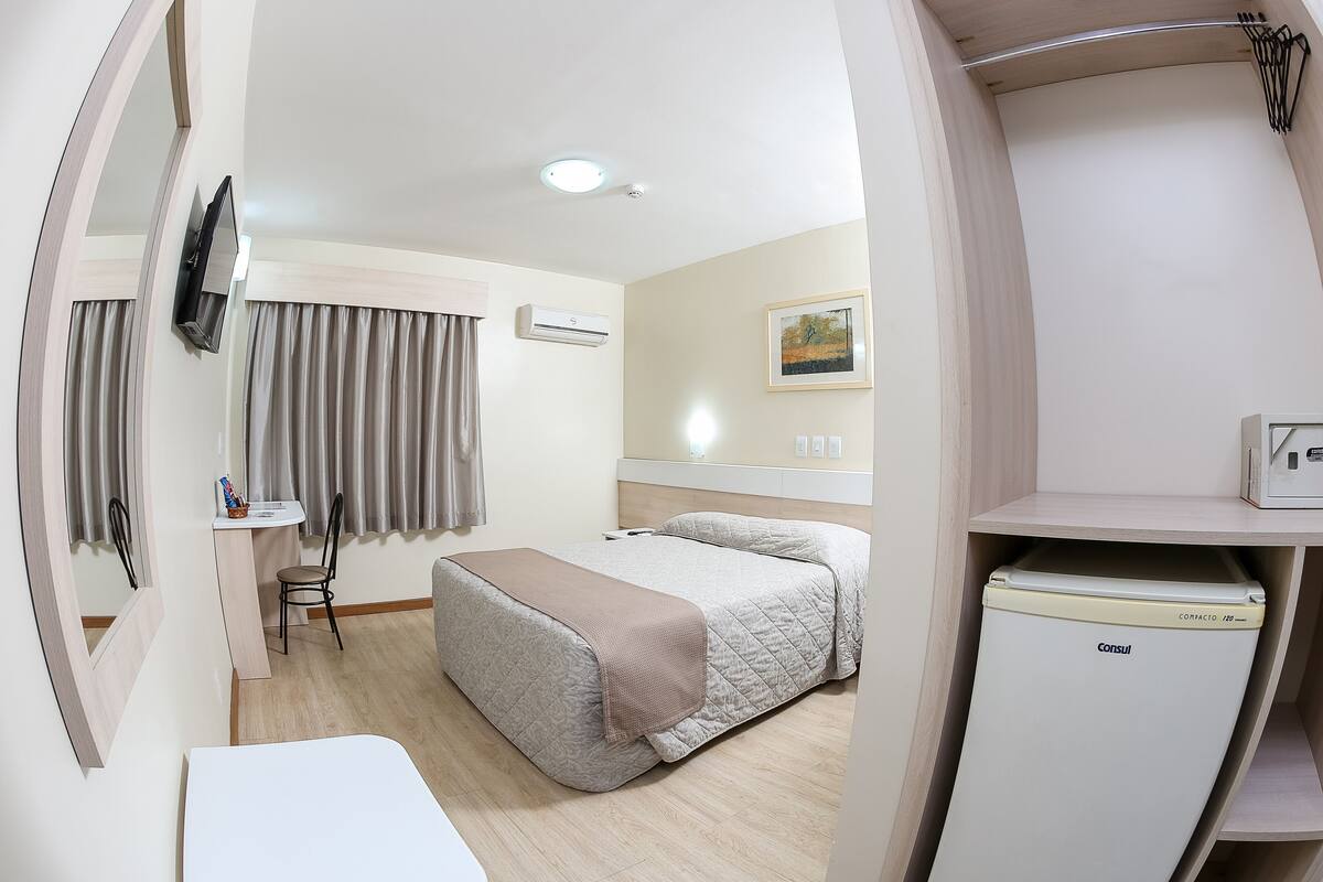 Ein Hotelzimmer mit Bett, Schreibtisch, Stuhl, Klimaanlage, Fernseher und Kühlschrank.