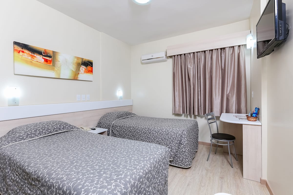 Ein Hotelzimmer mit zwei Betten, einem Schreibtisch, einem Sessel, einem Fernseher und einem Bild an der Wand.