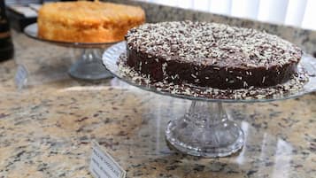 A chocolate cake with sprinkles on a glass cake stand on a granite countertop.