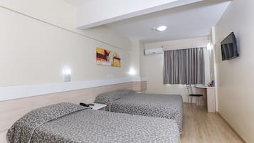 Habitación de hotel con dos camas, un escritorio, una silla, un aire acondicionado y un televisor en la pared.