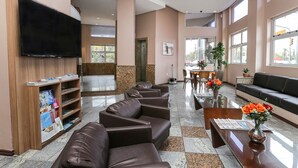 Un vestíbulo de hotel con sofás de cuero, un televisor de pantalla plana, un mostrador de recepción y un área de comedor.