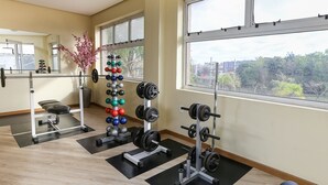 Un gimnasio con equipo de levantamiento de pesas, una banca y un amplio ventanal con vistas a la ciudad.