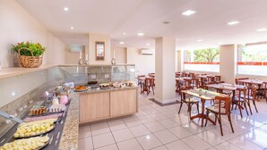 A buffet area with various food items, a kitchen counter, and a dining area with tables and chairs. - Hotel Suárez Executive Novo Hamburgo (Novo Hamburgo)
