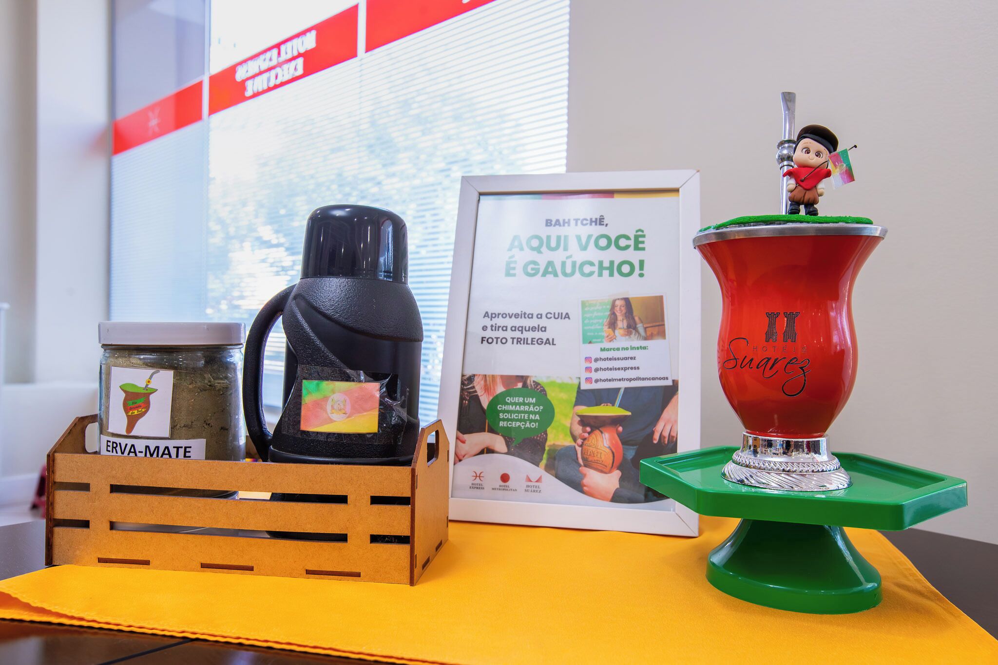 Una cafetera, un tarro etiquetado como 'ERVA-MATE' y un cartel enmarcado con una fotografía y texto.