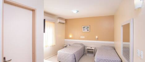 Une chambre d’hôtel avec deux lits, un bureau, une chaise, une fenêtre avec des rideaux et un climatiseur fixé au mur.