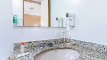 Un baño con encimera de granito, un lavabo, un espejo y un secador de pelo fijado a la pared.
