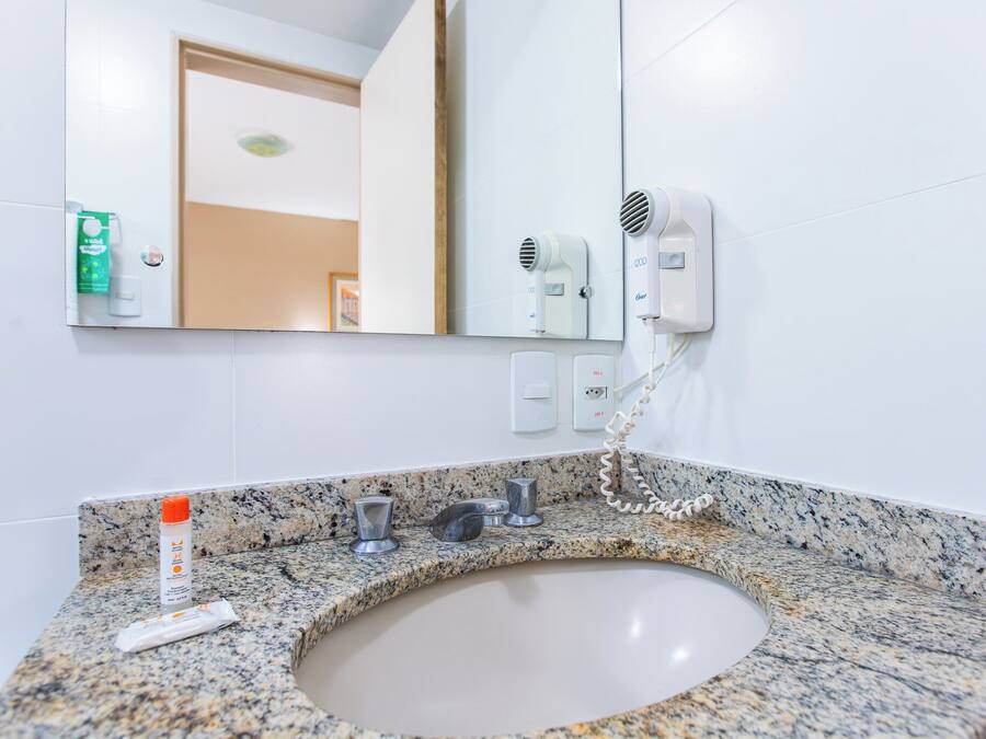 Un baño con encimera de granito, un lavabo, un espejo y un secador de pelo fijado a la pared.