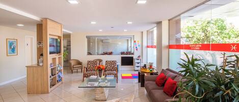 A modern living room with a glass coffee table, two sofas, a bookshelf, and a TV.