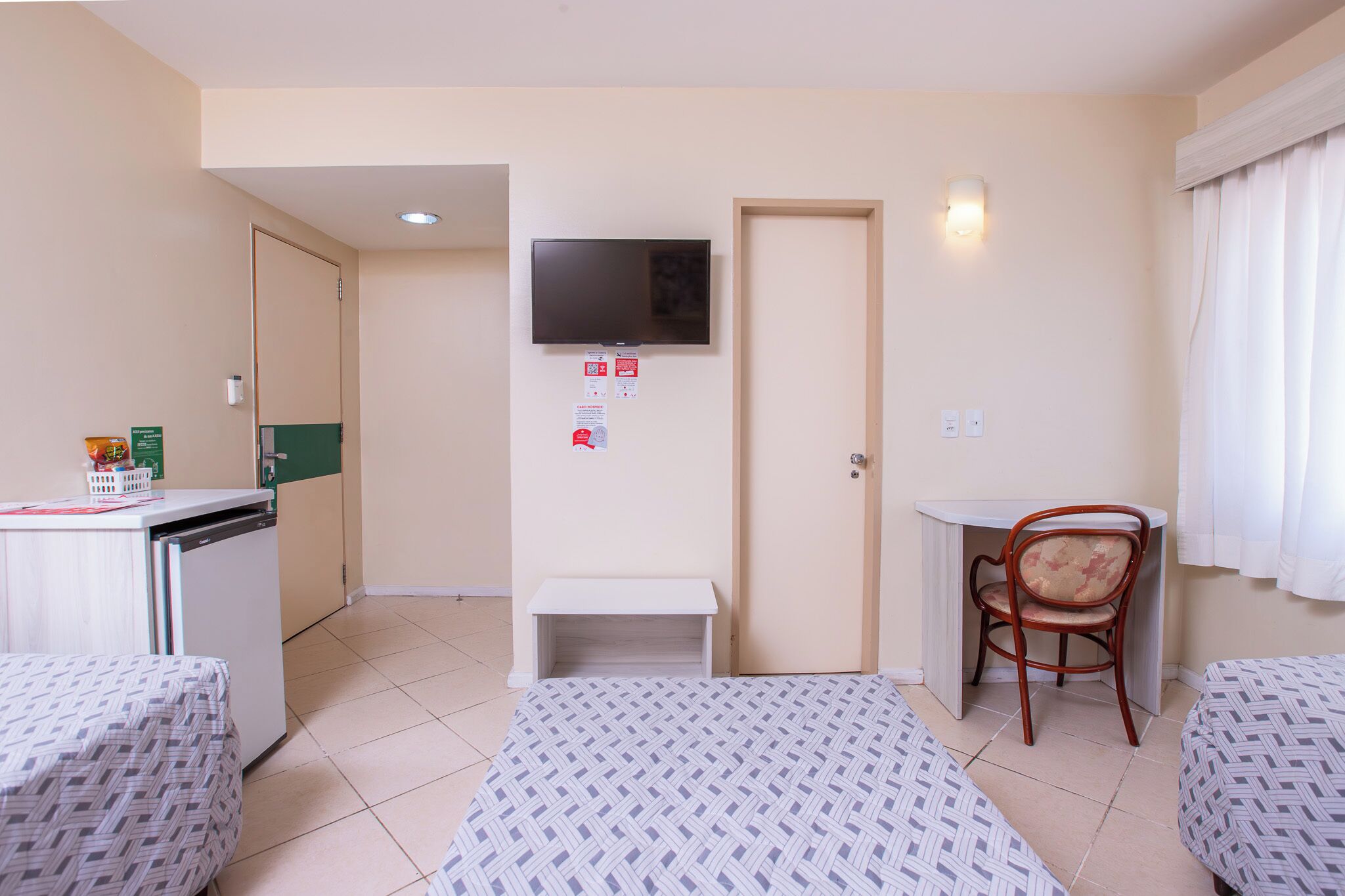 A hotel room with two beds, a desk, a chair, a television, and a small table.