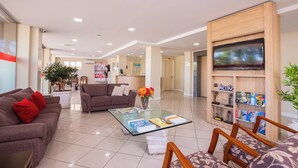 A hotel lobby with a glass coffee table, sofas, a TV, and a bookshelf. - Hotel Suárez Executive Novo Hamburgo (Novo Hamburgo)