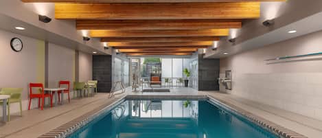 A swimming pool with a wooden ceiling, a clock, and seating areas with chairs.