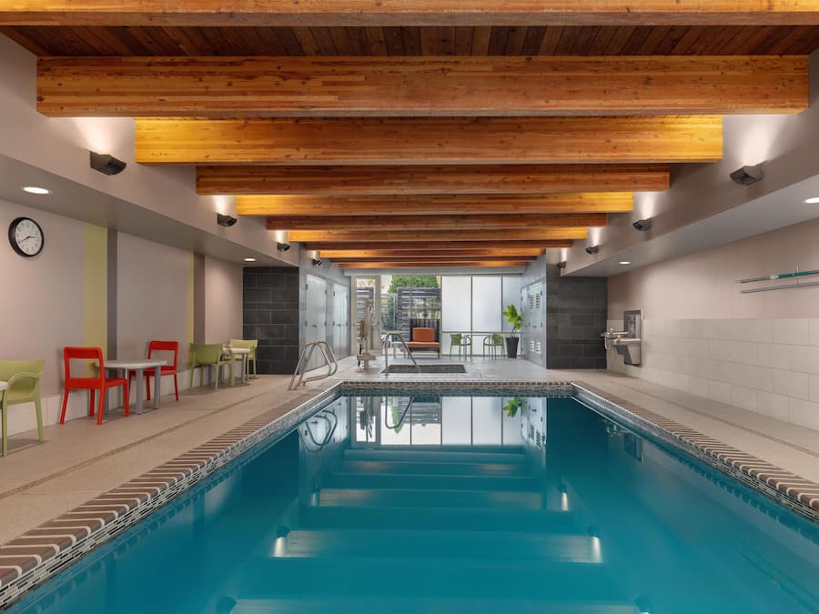 A swimming pool with a wooden ceiling, a clock, and seating areas with chairs.