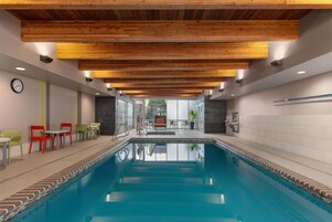 Una piscina con techo de madera, un reloj y zonas de estar con sillas.