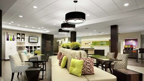 A modern hotel lobby with a sofa, chairs, a coffee bar, and a reception desk. - Home2 Suites by Hilton Salt Lake City/West Valley City, UT (West Valley City)