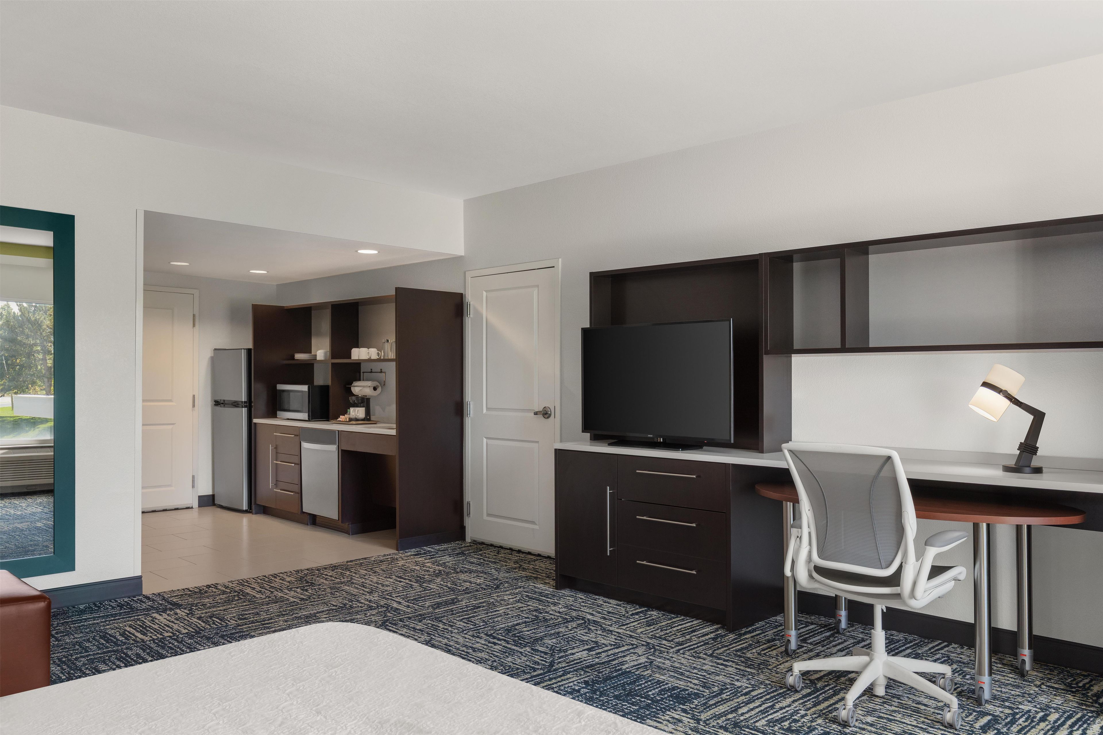 A modern hotel room with a large bed, a desk with a computer, a flat-screen TV, and a seating area with a chair.