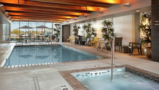 An indoor swimming pool with clear water, wooden ceiling beams, and a view of the outside. - Home2 Suites by Hilton Salt Lake City/West Valley City, UT (West Valley City)