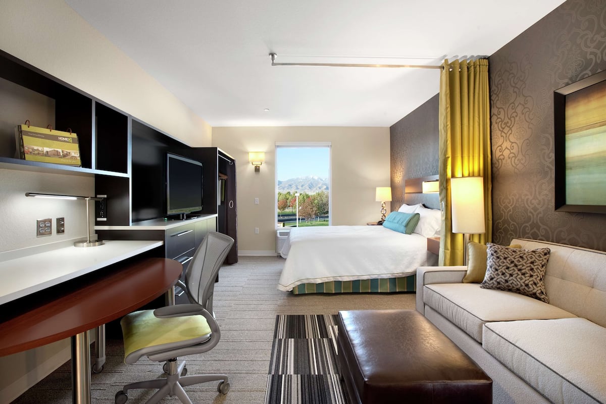 A hotel room with a desk, chair, bed, sofa, and a view of mountains.