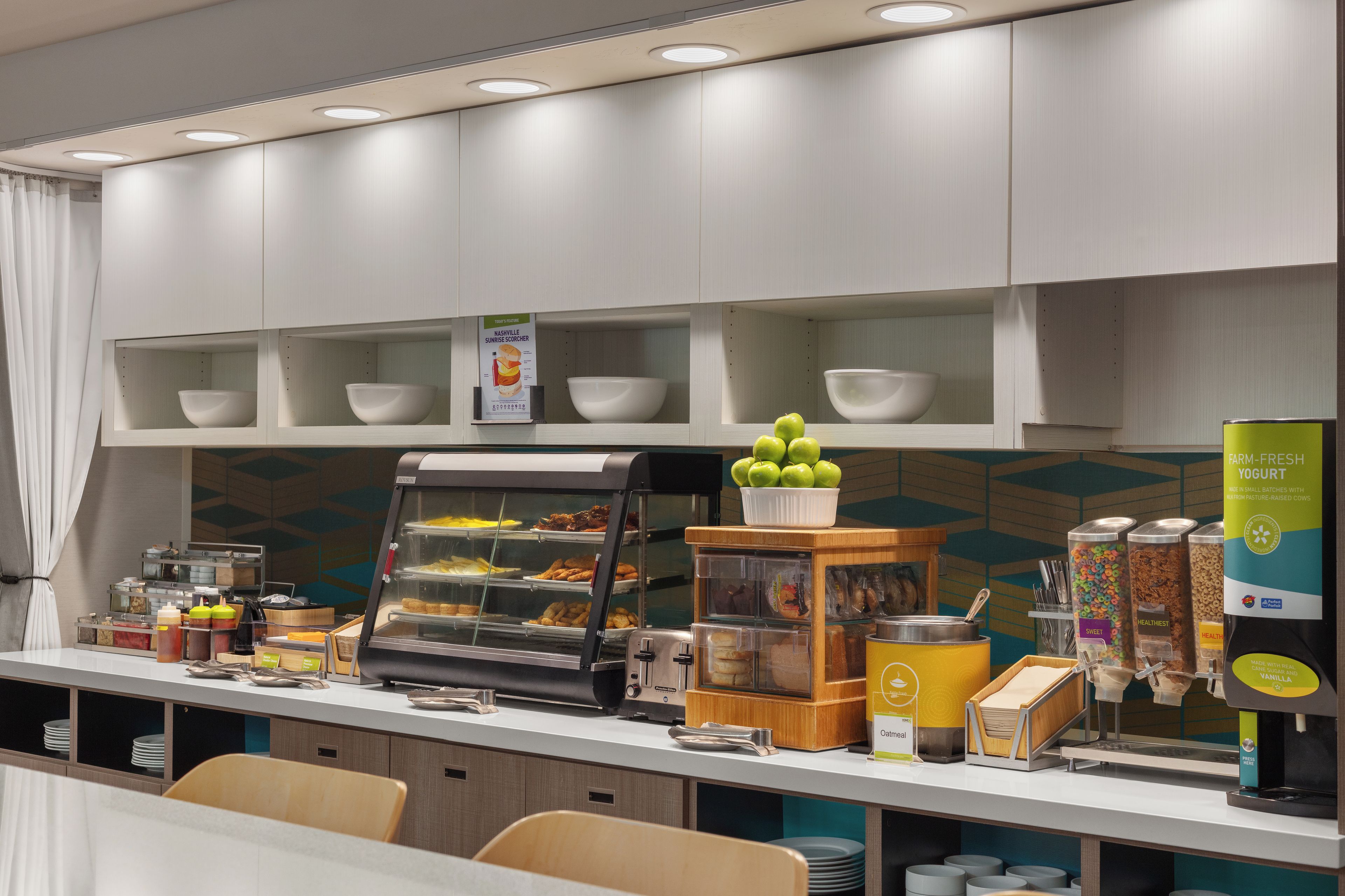 Una barra de desayuno con diversas opciones de comida, incluyendo un expositor con pasteles y una máquina de café.