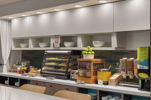 Una barra de desayuno con diversas opciones de comida, incluyendo un expositor con pasteles y una máquina de café.